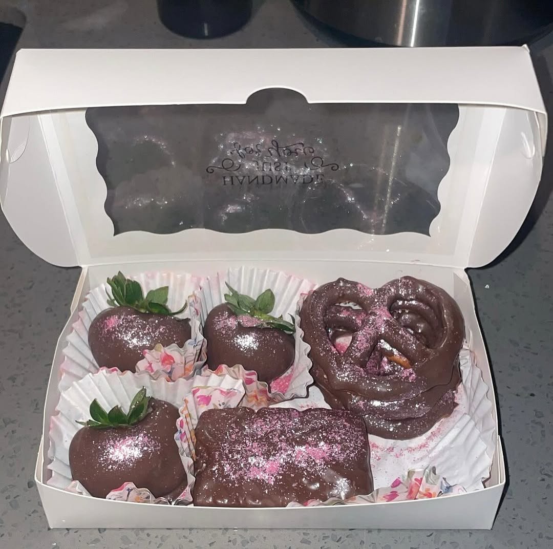 Small sampler box with three pink-shimmer strawberries, a chocolate pretzel, and a Rice Krispie bar, all with pink edible glitter and floral liners.