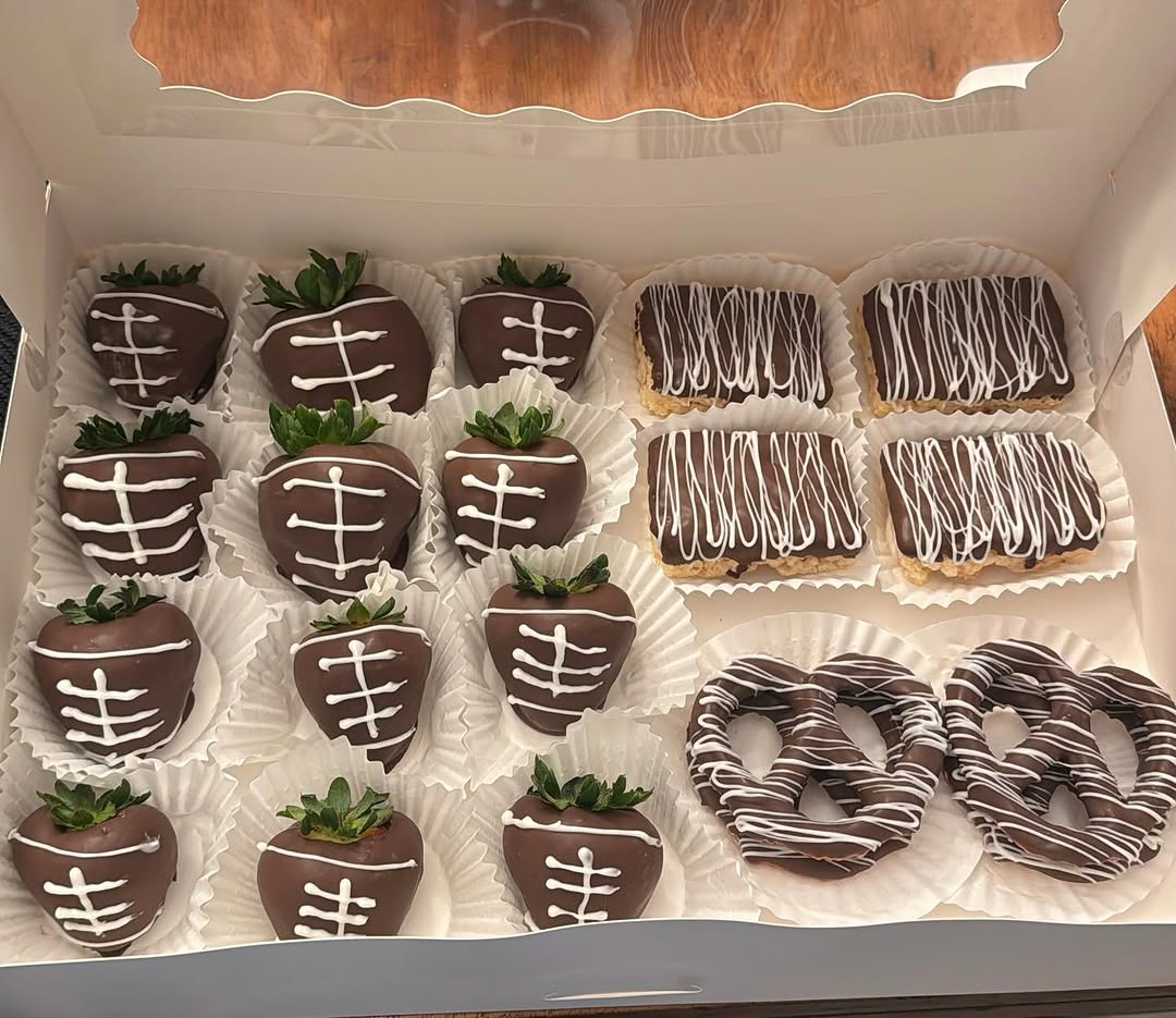 Football-themed treat box with twelve dark chocolate strawberries decorated with white piped laces, plus drizzled Rice Krispie bars and pretzels.