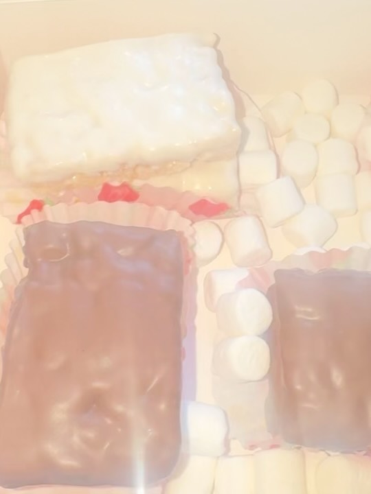 Close-up of glossy chocolate-coated mushroom-shaped marshmallow pops with pink accent liners and scattered mini marshmallows.
