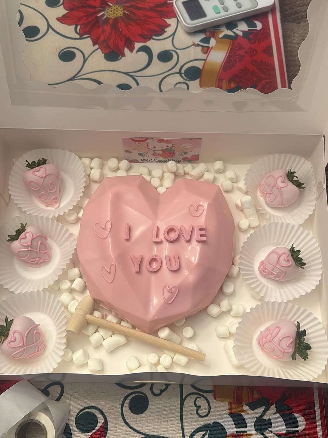 Valentine's Day breakable pink heart with I LOVE YOU text, four pink drizzled strawberries, a wooden mallet, and mini marshmallows in a white bakery box.