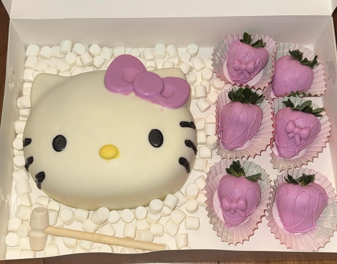 Hello Kitty breakable chocolate shell with pink bow and six matching lavender Hello Kitty-themed strawberries, with a wooden mallet for smashing.