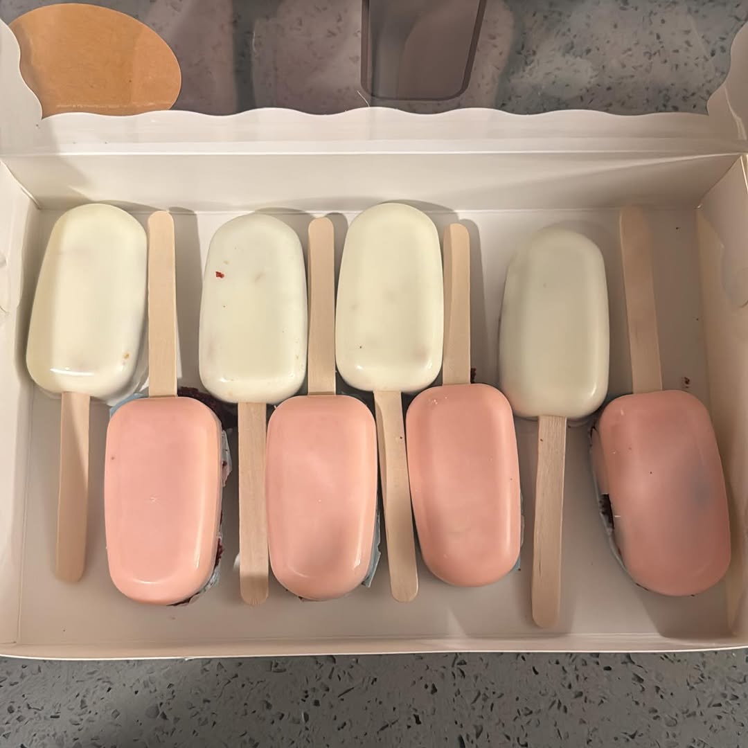 Eight minimalist cakesicles in alternating white ivory and soft pink peach, with smooth glossy coatings for an elegant presentation.