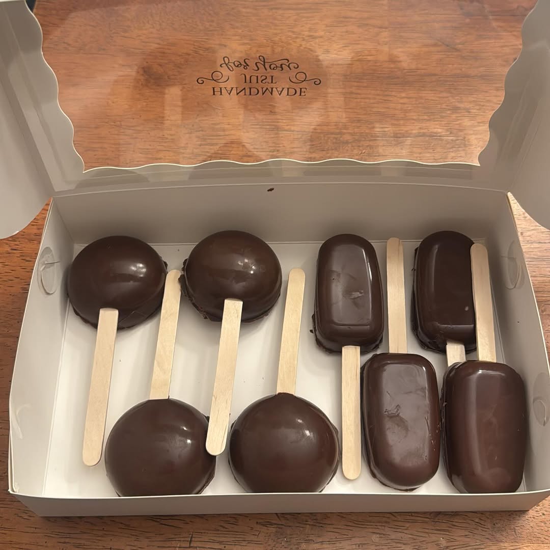 Eight dark chocolate cake pops and cakesicles in round and rectangular shapes, providing visual variety in a monochrome presentation.