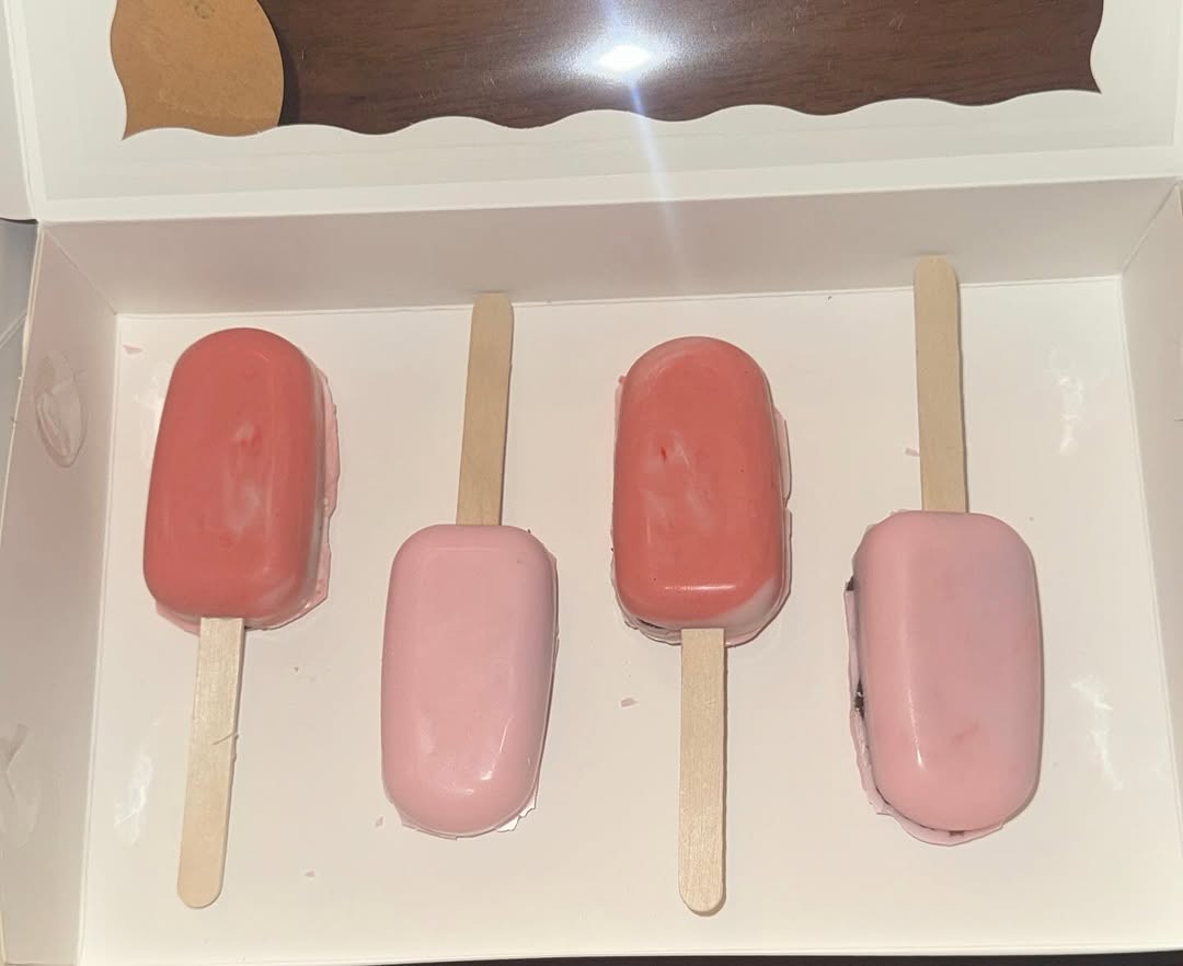Four minimalist cakesicles in alternating coral pink and baby pink shades with smooth glossy candy coating.
