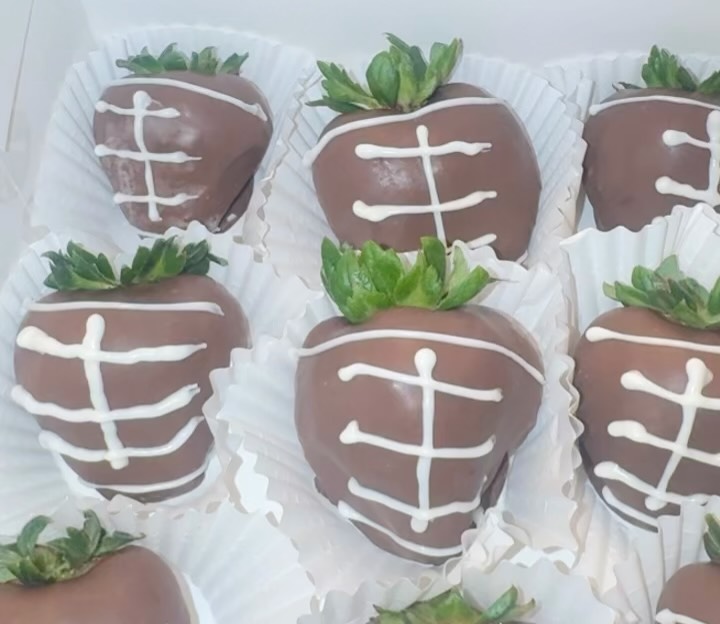 Close-up of chocolate-covered strawberries decorated as footballs with white chocolate piped lace stitching detail.
