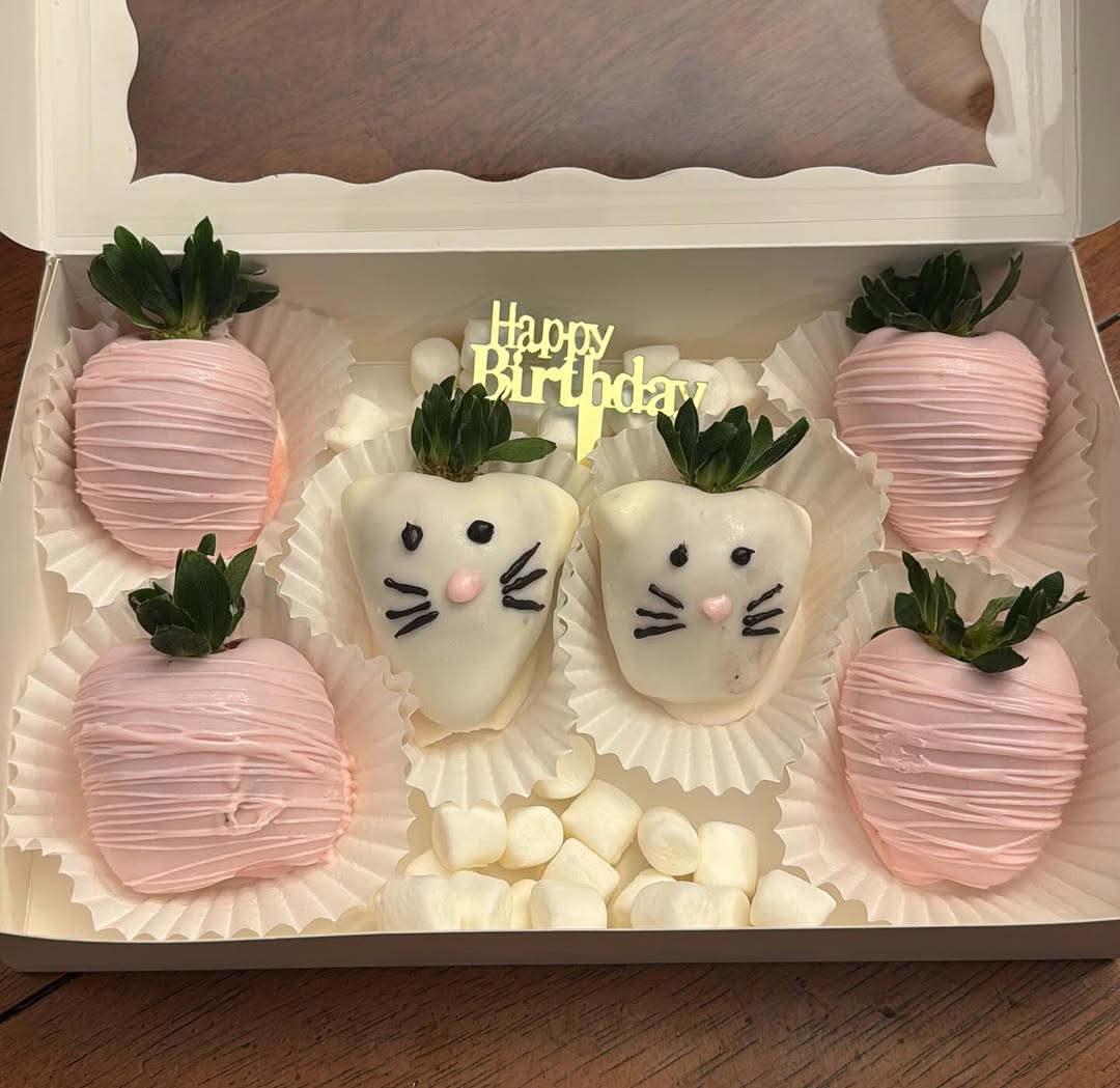 Birthday box with four pink drizzled strawberries and two white chocolate cat-face strawberries with whiskers, plus a gold Happy Birthday topper.